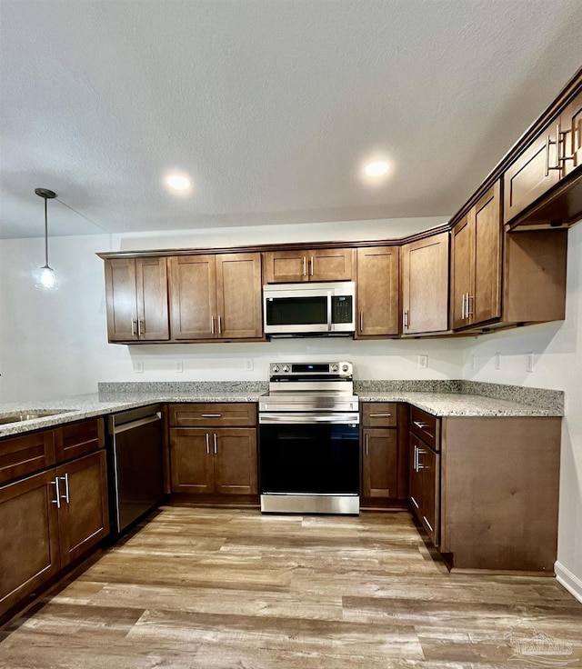 kitchen with light stone counters, light wood-style floors, appliances with stainless steel finishes, and a sink