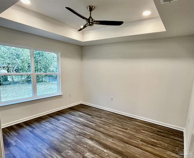 spare room with ornamental molding, a ceiling fan, a tray ceiling, dark wood finished floors, and baseboards