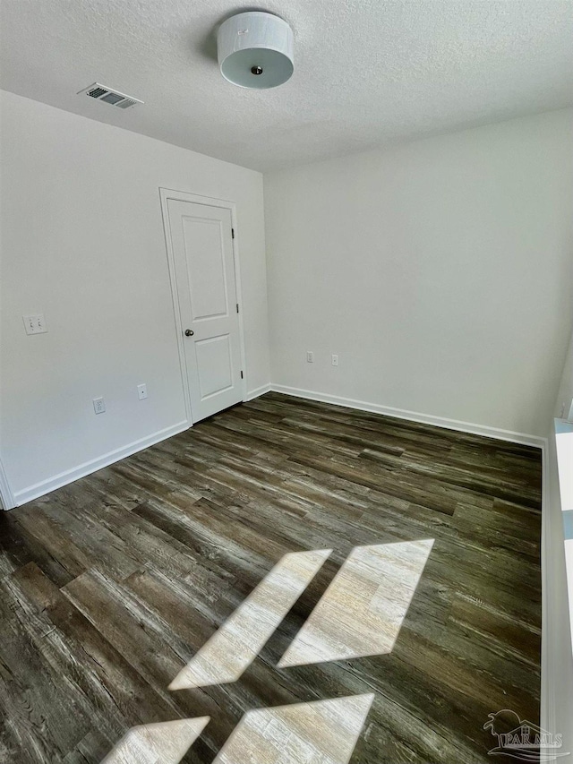 empty room featuring visible vents, baseboards, a textured ceiling, and dark wood finished floors