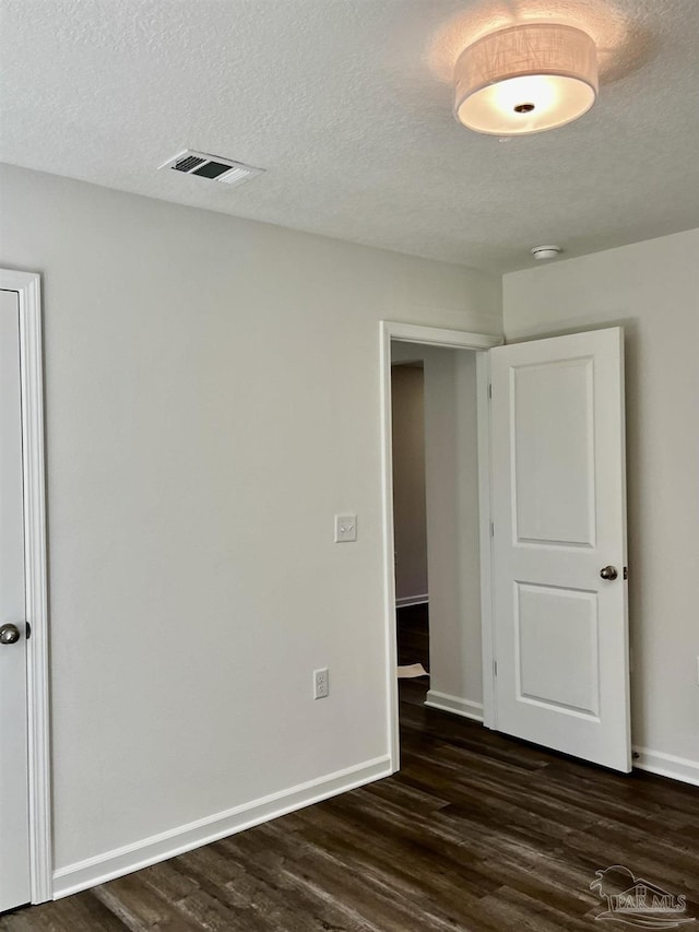 unfurnished room with dark wood-style floors, visible vents, a textured ceiling, and baseboards