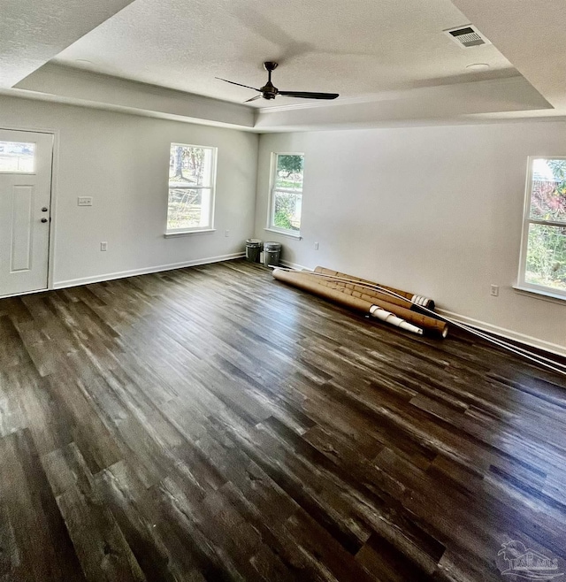 interior space featuring dark wood finished floors, a tray ceiling, a healthy amount of sunlight, and visible vents