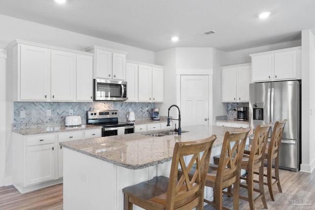 kitchen with appliances with stainless steel finishes, a kitchen island with sink, and white cabinets