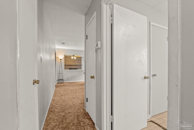 hallway featuring light colored carpet and a textured ceiling