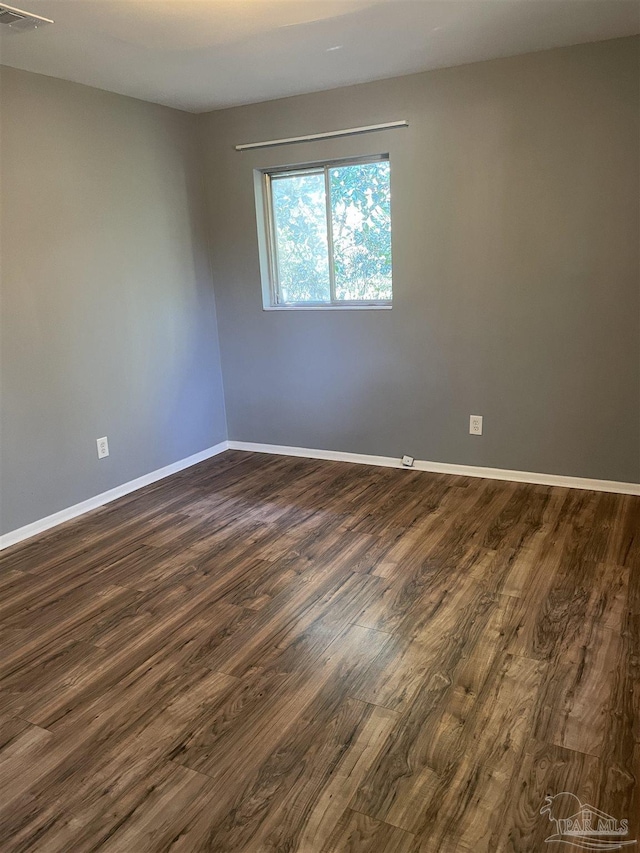 empty room with dark wood-style flooring, visible vents, and baseboards