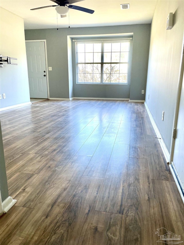 empty room with baseboards, ceiling fan, visible vents, and dark wood-type flooring