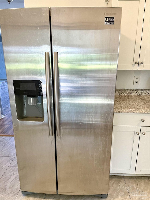 details featuring light stone countertops, stainless steel fridge, and white cabinetry