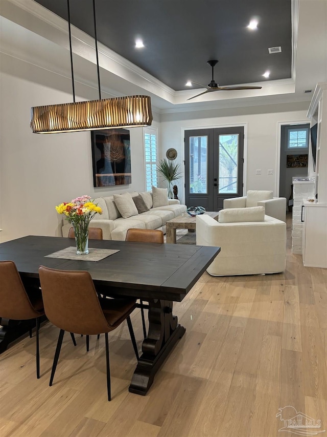 dining room featuring a tray ceiling, light wood-style floors, french doors, and ornamental molding