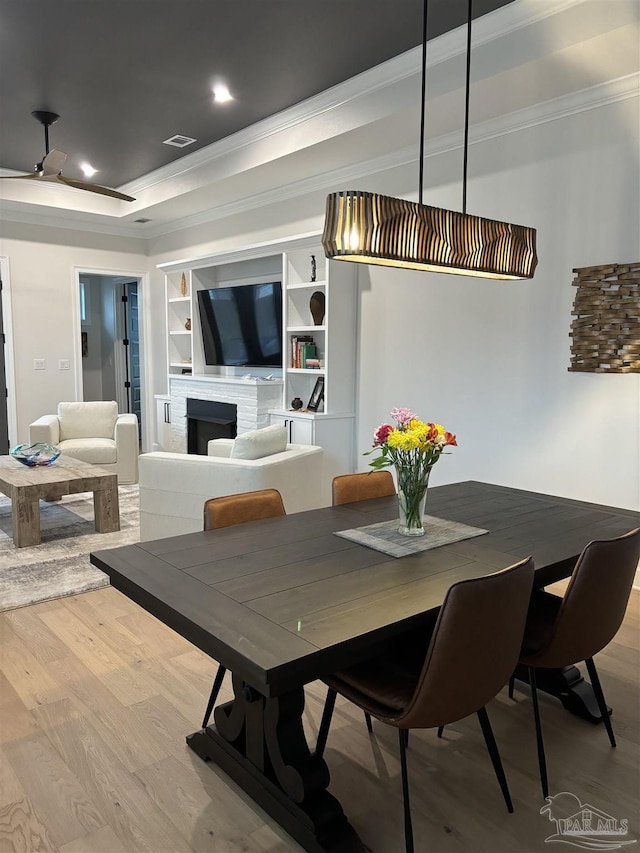 dining space with visible vents, a tray ceiling, a fireplace, crown molding, and light wood-type flooring