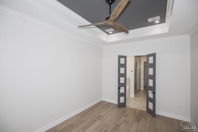 unfurnished room featuring wood finished floors, visible vents, a tray ceiling, ceiling fan, and ornamental molding