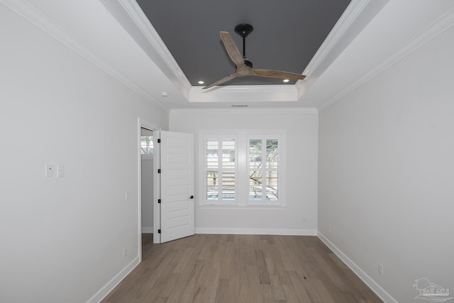 spare room featuring a raised ceiling, wood finished floors, baseboards, and ornamental molding