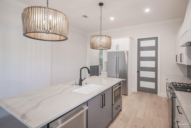 kitchen featuring ornamental molding, stainless steel appliances, a sink, white cabinetry, and light wood-type flooring