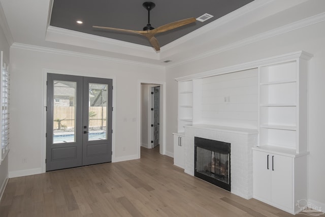 foyer entrance with french doors, light wood-style floors, crown molding, a raised ceiling, and a brick fireplace