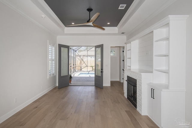 entryway with a raised ceiling, light wood-style floors, a fireplace, and crown molding