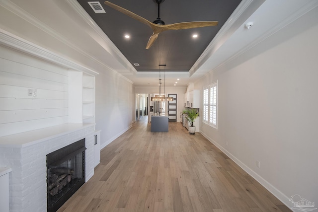 unfurnished living room featuring visible vents, a tray ceiling, a fireplace, ornamental molding, and light wood-type flooring