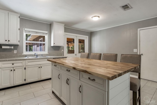 6845 Trail Ride S, Milton, FL 32570 - kitchen featuring butcher block countertops, a kitchen bar, light tile patterned floors, white cabinets, and ornamental molding