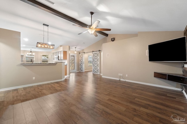 unfurnished living room with baseboards, dark wood finished floors, lofted ceiling with beams, a barn door, and ceiling fan with notable chandelier