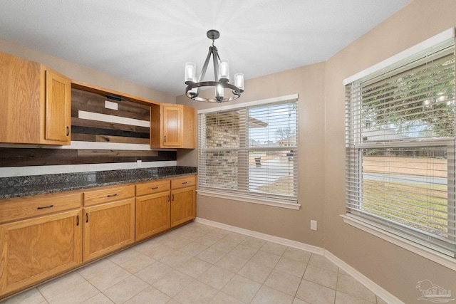 kitchen featuring a notable chandelier, dark stone countertops, light tile patterned floors, baseboards, and hanging light fixtures