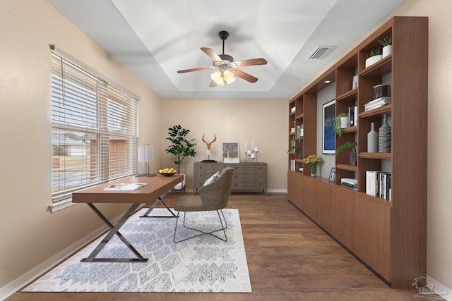 office space featuring a ceiling fan, wood finished floors, visible vents, baseboards, and a raised ceiling