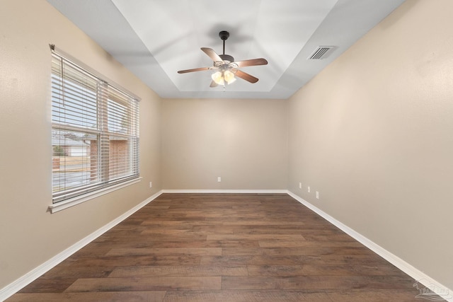 empty room with a raised ceiling, baseboards, dark wood-type flooring, and visible vents