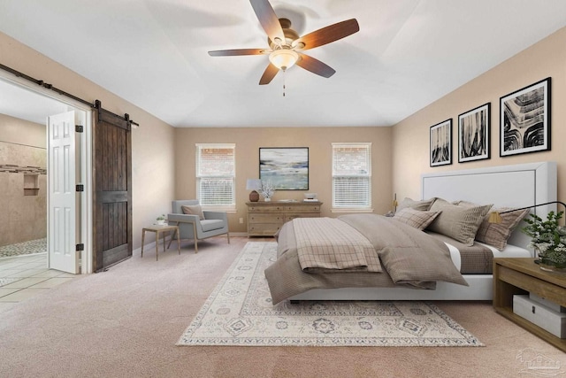 bedroom with baseboards, carpet, a barn door, ensuite bath, and a ceiling fan