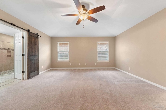 unfurnished bedroom featuring baseboards, a barn door, vaulted ceiling, carpet floors, and a ceiling fan