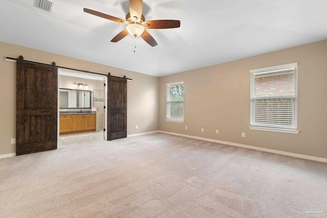 unfurnished bedroom with visible vents, baseboards, ensuite bath, a barn door, and light colored carpet