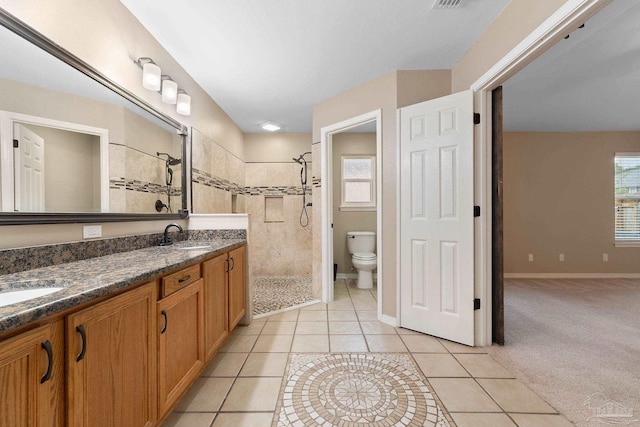 bathroom with double vanity, a tile shower, a sink, tile patterned flooring, and toilet