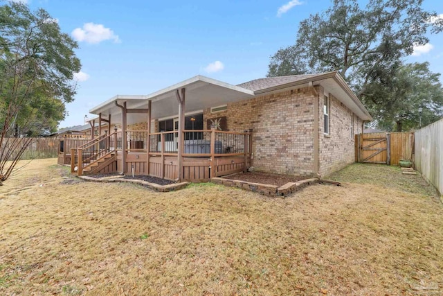 rear view of property featuring a yard, brick siding, a fenced backyard, and a gate