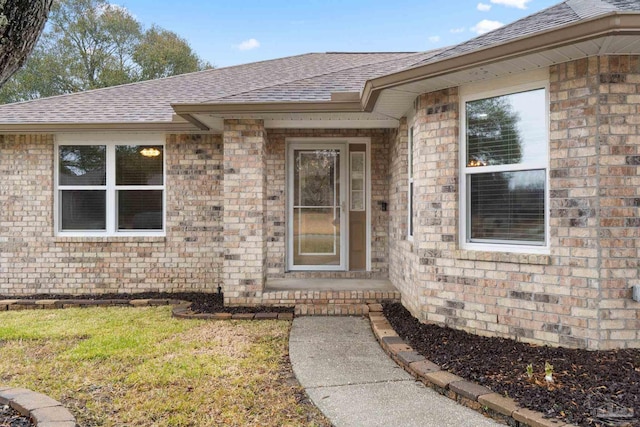 view of exterior entry with brick siding and roof with shingles