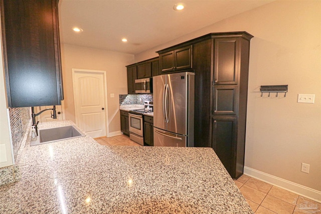 kitchen featuring light stone countertops, appliances with stainless steel finishes, dark brown cabinetry, sink, and backsplash