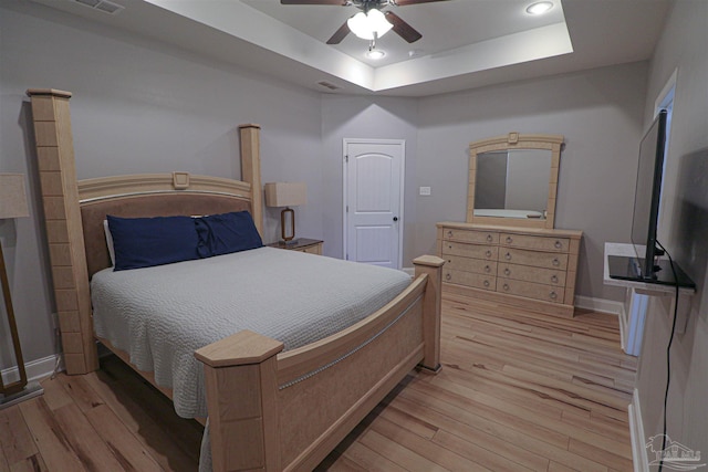 bedroom with ceiling fan, light hardwood / wood-style flooring, and a raised ceiling