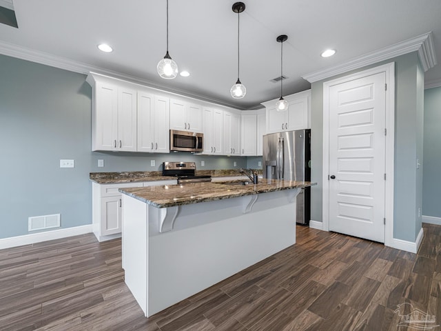 kitchen featuring dark hardwood / wood-style flooring, appliances with stainless steel finishes, an island with sink, dark stone countertops, and white cabinets