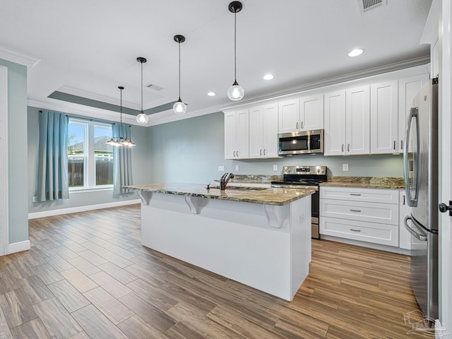 kitchen with white cabinets, light hardwood / wood-style flooring, appliances with stainless steel finishes, stone countertops, and an island with sink