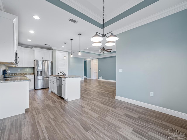 kitchen with a kitchen island with sink, a raised ceiling, ceiling fan with notable chandelier, hanging light fixtures, and appliances with stainless steel finishes