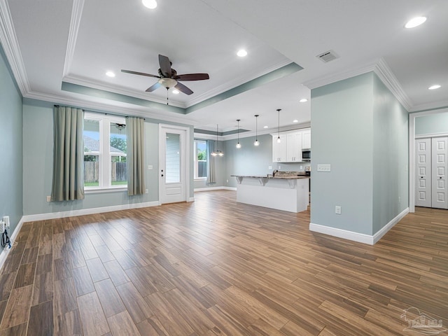 unfurnished living room with a raised ceiling, ceiling fan, ornamental molding, and hardwood / wood-style flooring