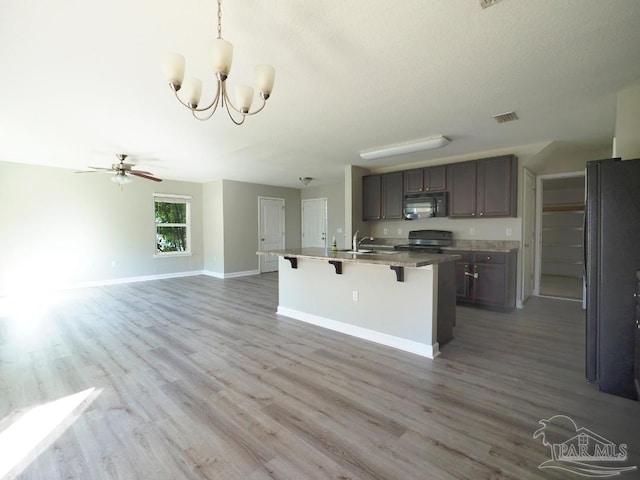 kitchen with black appliances, light wood-type flooring, decorative light fixtures, a breakfast bar, and a kitchen island with sink