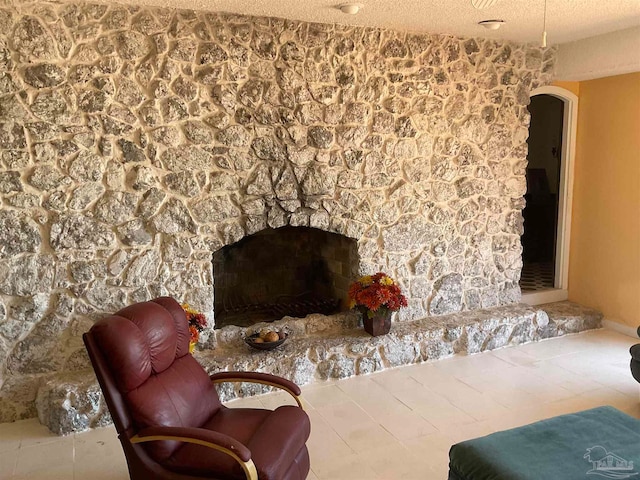 living area featuring tile patterned flooring, a textured ceiling, and a stone fireplace