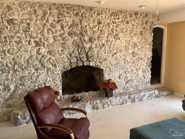 living area with a stone fireplace and a textured ceiling