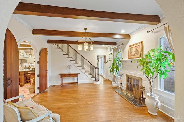 living room with a notable chandelier, beam ceiling, light hardwood / wood-style flooring, and ornamental molding