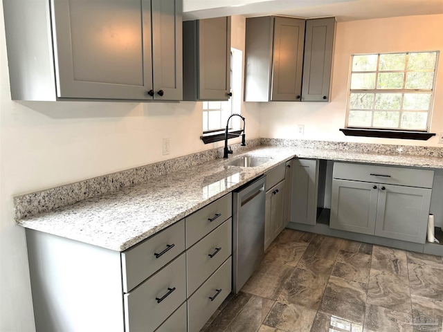 kitchen with stainless steel dishwasher, gray cabinets, sink, and light stone countertops