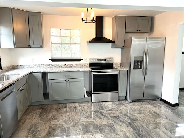 kitchen featuring stainless steel appliances, decorative light fixtures, sink, light stone counters, and wall chimney range hood