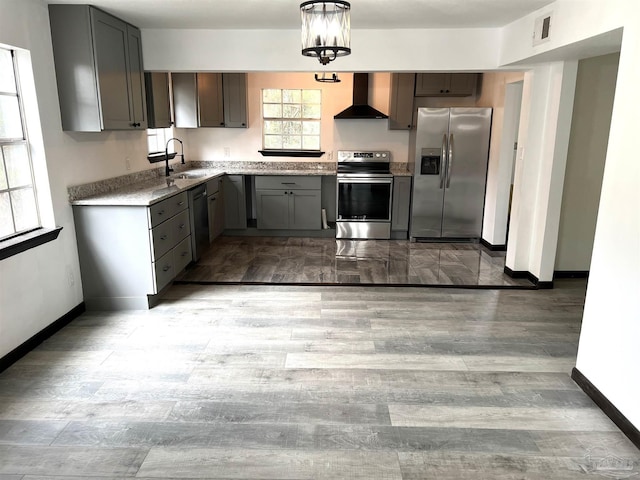 kitchen with appliances with stainless steel finishes, hardwood / wood-style flooring, wall chimney exhaust hood, pendant lighting, and sink