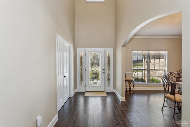 entrance foyer featuring baseboards, dark wood-type flooring, a towering ceiling, and arched walkways