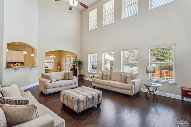 living area featuring arched walkways, dark wood finished floors, and baseboards