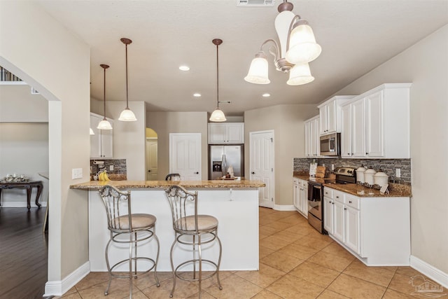 kitchen featuring light tile patterned floors, stainless steel appliances, arched walkways, and a peninsula