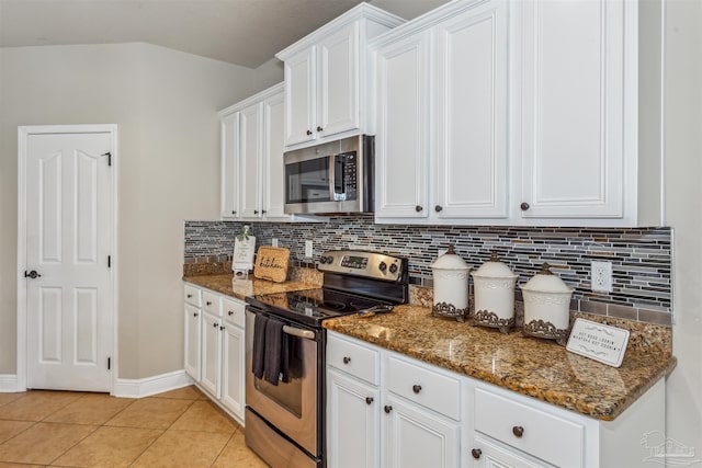 kitchen with stainless steel appliances, dark stone counters, white cabinets, light tile patterned floors, and decorative backsplash