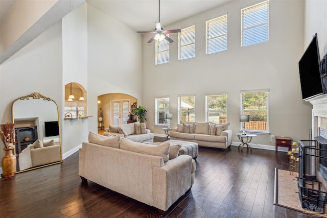 living room featuring arched walkways, a fireplace with flush hearth, dark wood-type flooring, and baseboards