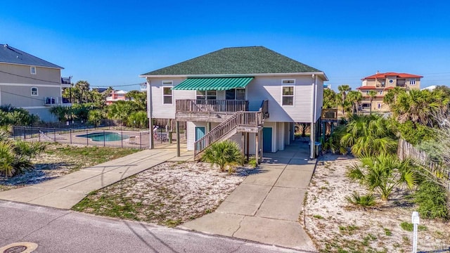 coastal inspired home with stairs, roof with shingles, fence, and a fenced in pool