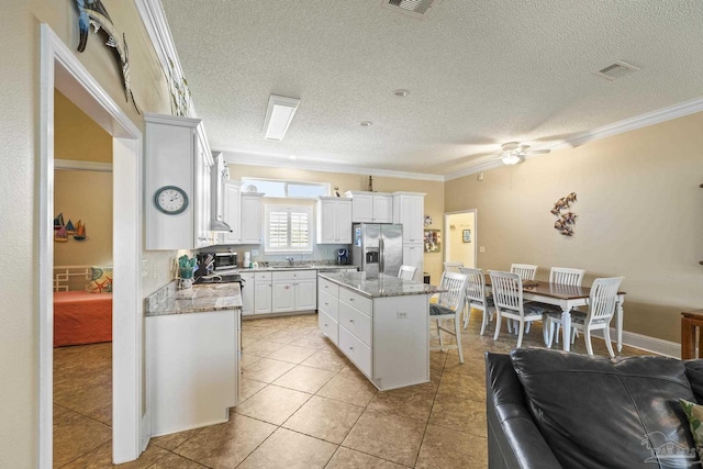 kitchen with stainless steel fridge, visible vents, ornamental molding, open floor plan, and a center island