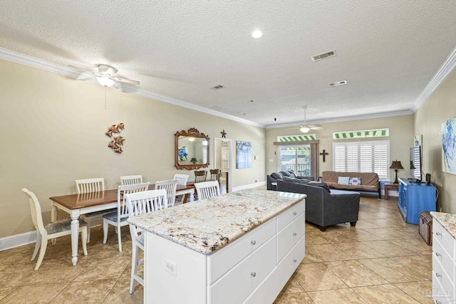 kitchen featuring ceiling fan, a kitchen island, white cabinetry, and crown molding